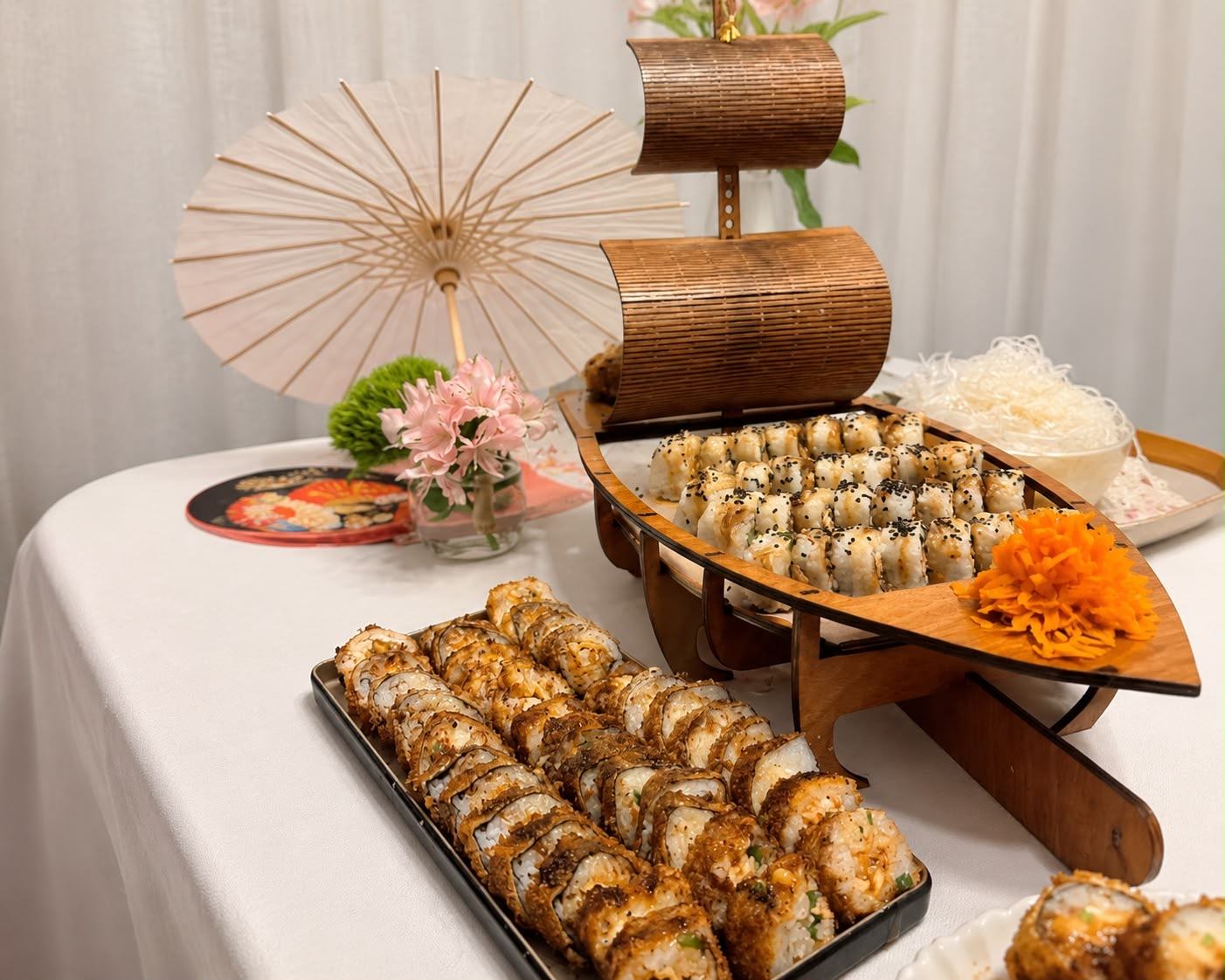 Mesa de evento montada por Emillo's con barco de sushi, sombrilla japonesa y flores